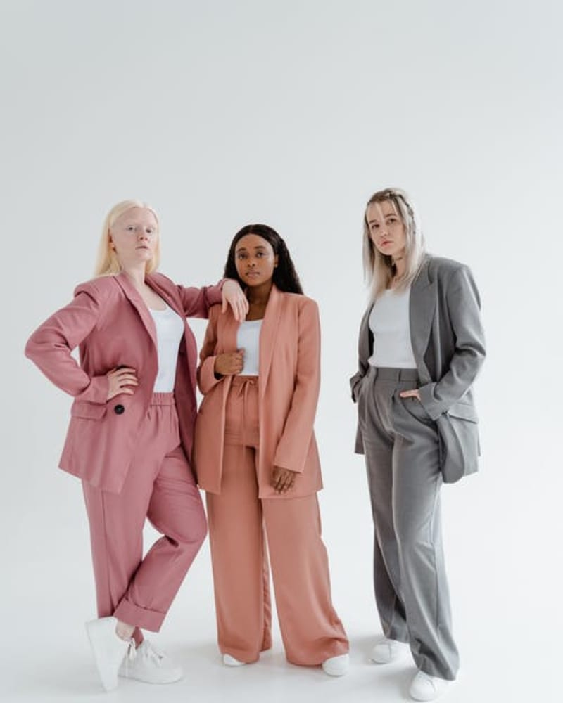 Three women in suits facing the camera, one pink, one orange and one grey