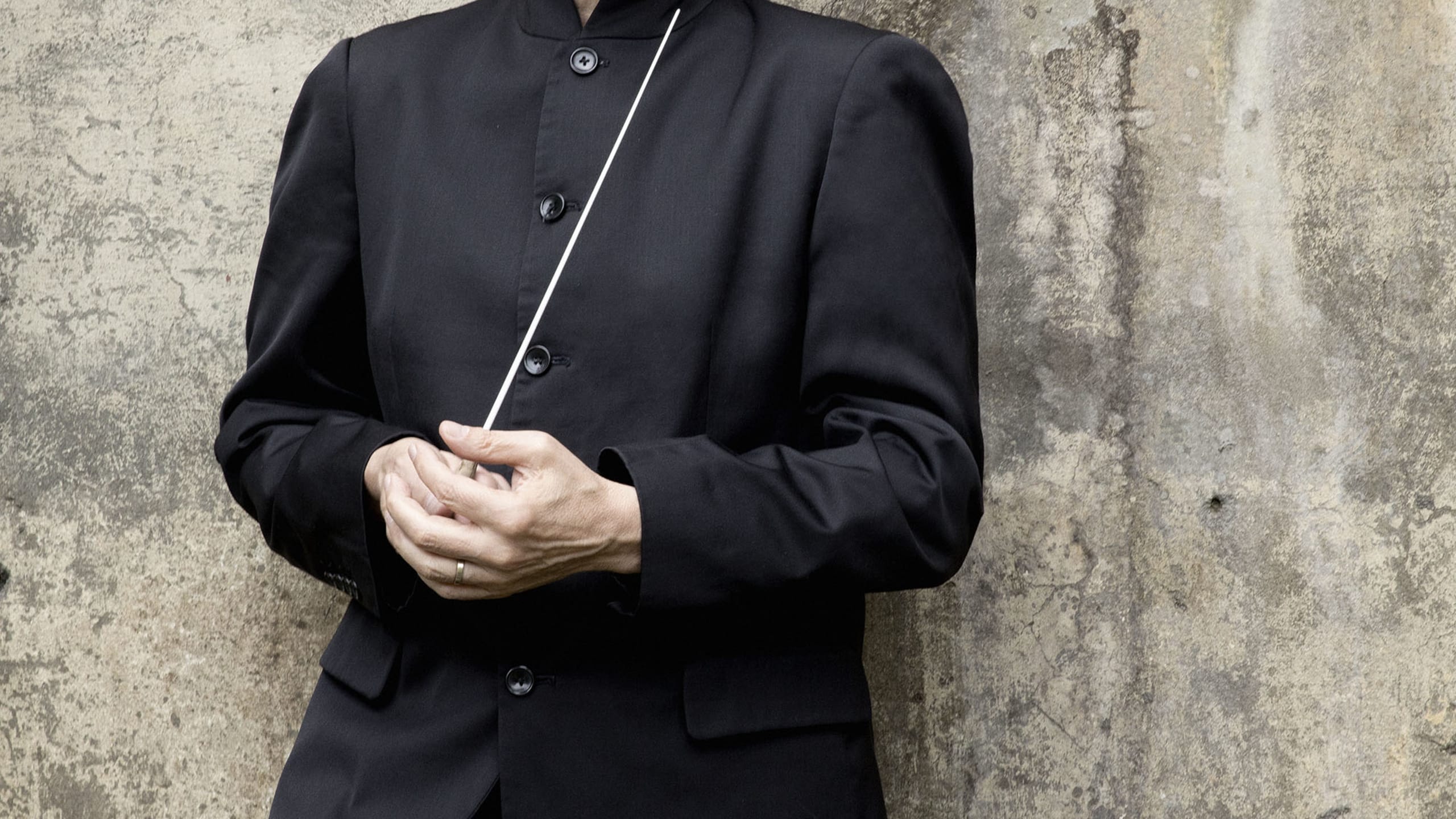 Portrait of conductor Osmo Vanska standing in front of wall holding a baton.