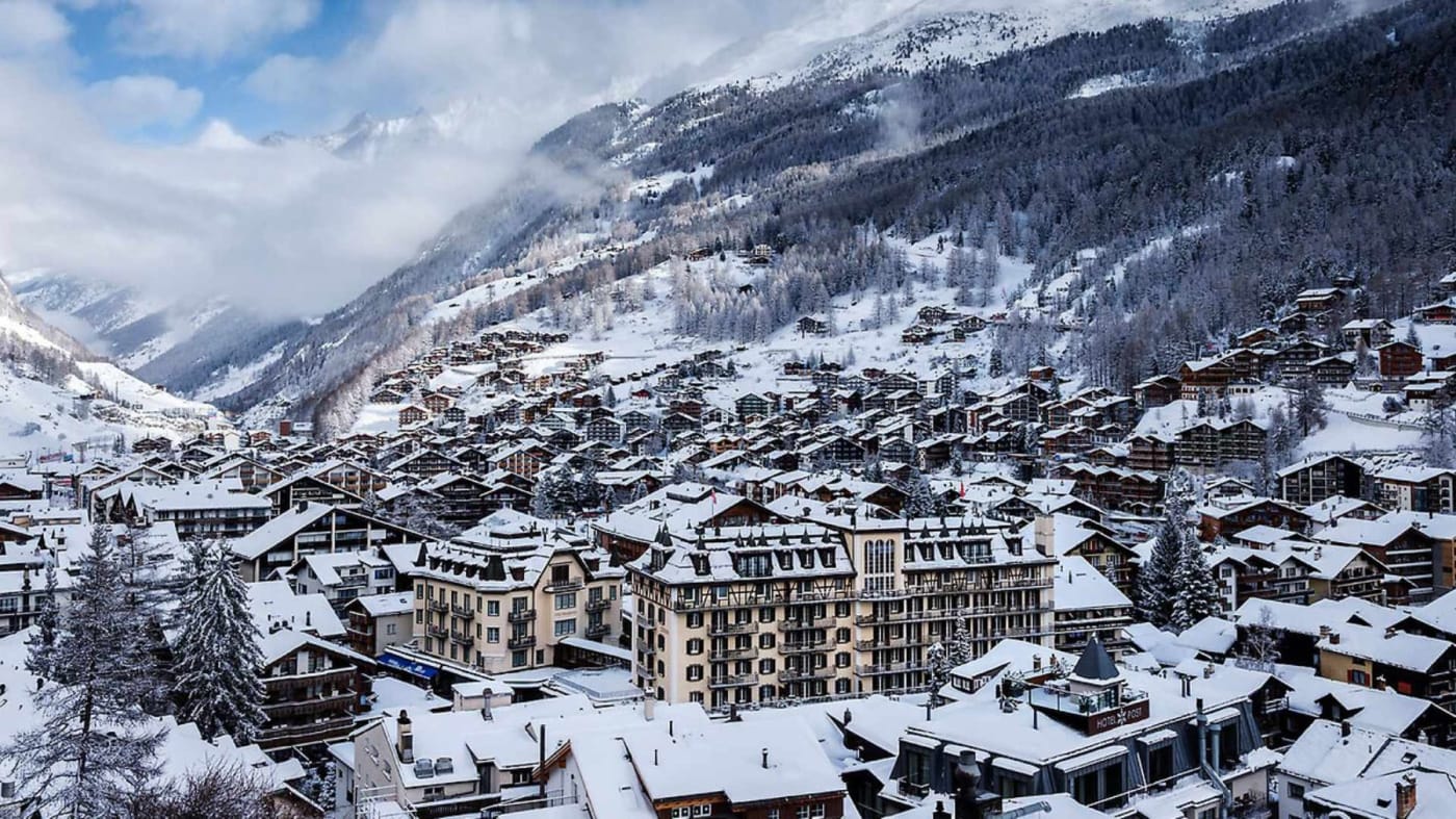 Das Mont Cervin Palace zwischen den verschneiten Dächern von Zermatt, am Fuß der Berge im Winter