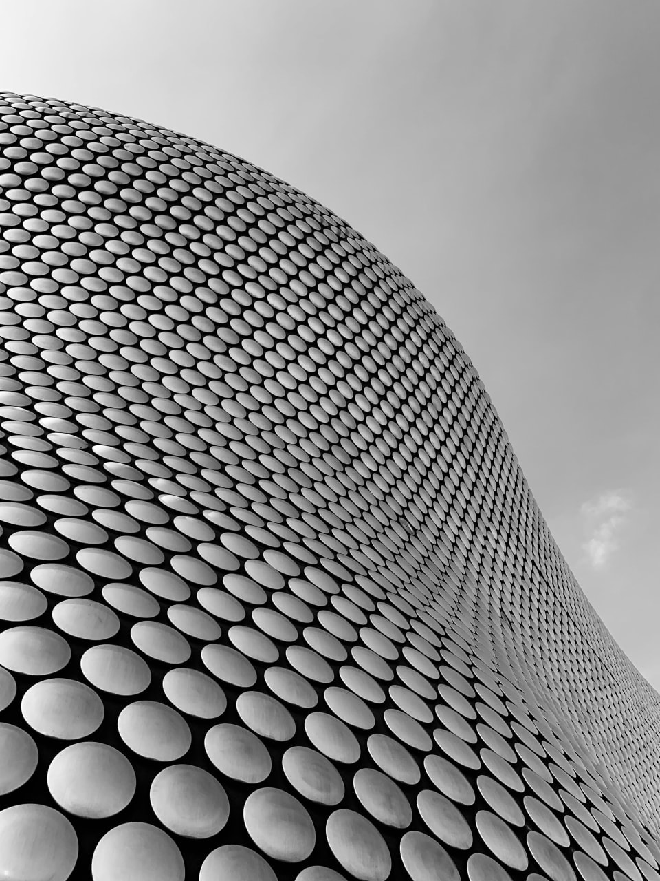 Architectural grayscale photo of a wavy sided building with circles on the side