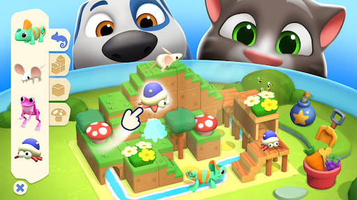 My Talking Tom Friends 2 26.5.0.25768 – Hank dan Tom membungkuk di atas mainan balok susun: taman kayu bertingkat dengan jamur, bunga, katak dan bunglon, serta palet balok di sisi kiri