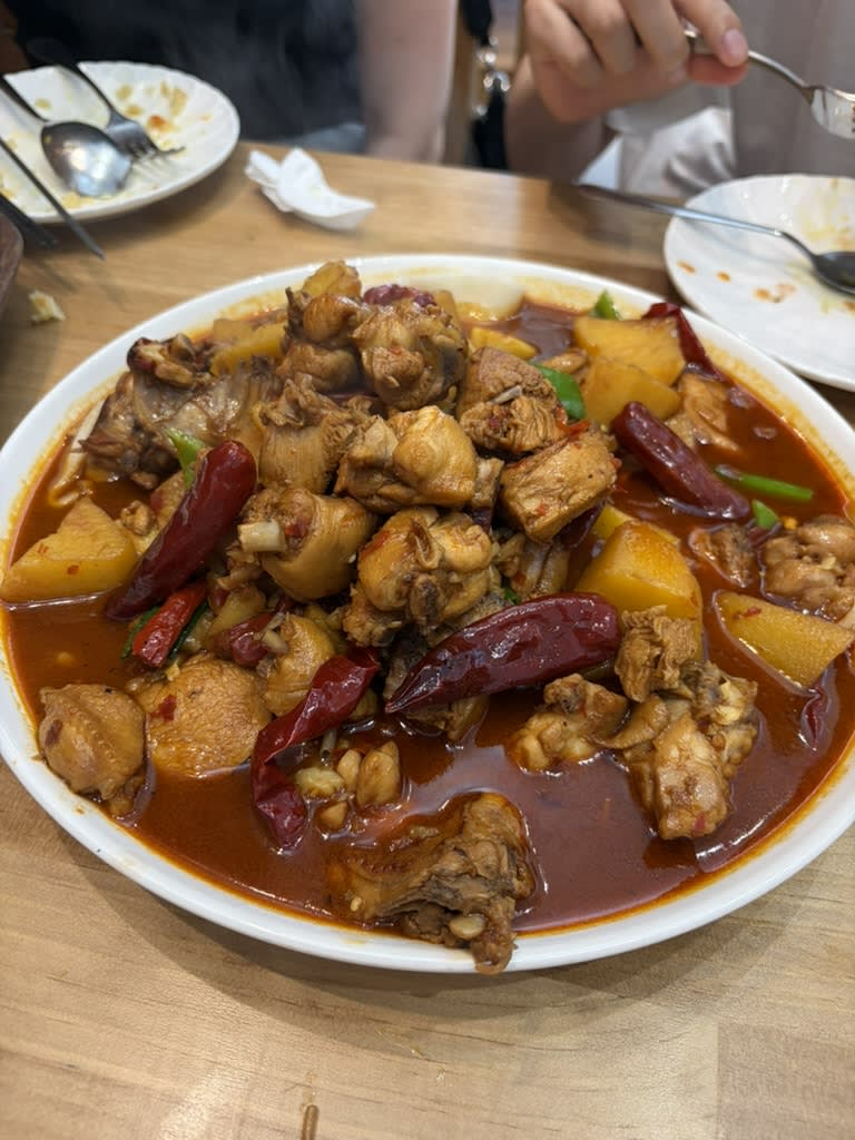 A large platter of Xinjiang big-plate chicken with bone-in pieces, potatoes, dried red chillies and green peppers in red sauce.