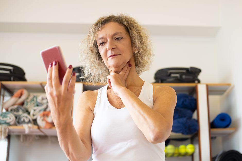 Oudere vrouw meet hartslag in nek met vingers, smartphone in hand