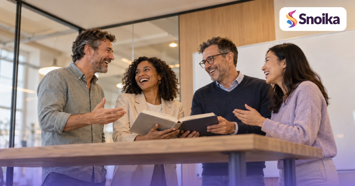 Four people in their forties in a glass-walled meeting room with a whiteboard.