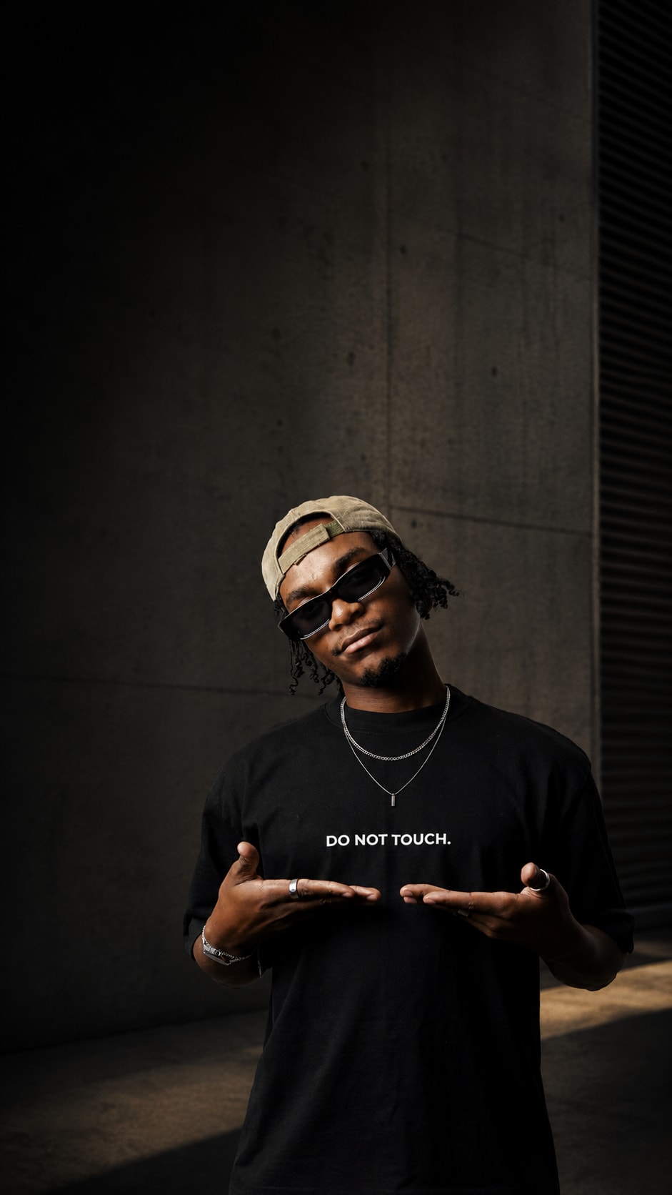 Do Not Touch model in sunglasses presenting the wordmark on an oversized black T-shirt against a concrete wall