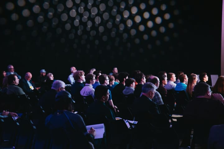 público sentado durante una charla en un auditorio oscuro