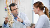 Doctor educating patient using spinal model.
