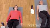 Two women lying on yoga mats doing a supine hamstring stretch.