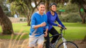 A woman riding a bicycle while a man runs along side her for exercise
