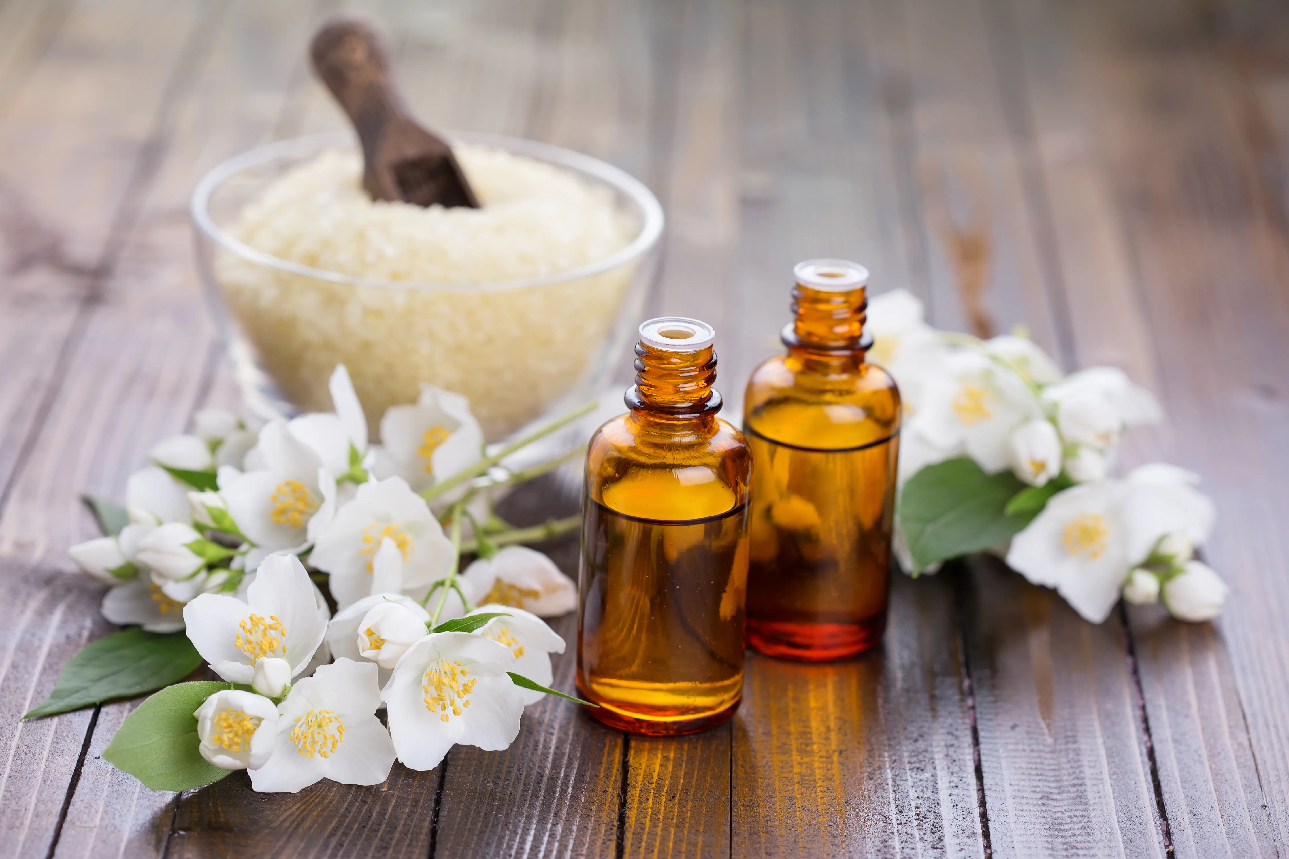 Small amber essential oil bottles with jasmine and spa elements on wooden surface