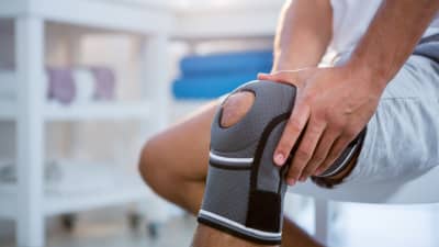 Man grabbing knee with a brace on.