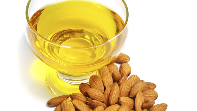 Bowl of almond oil surrounded in front of a bunch of almonds