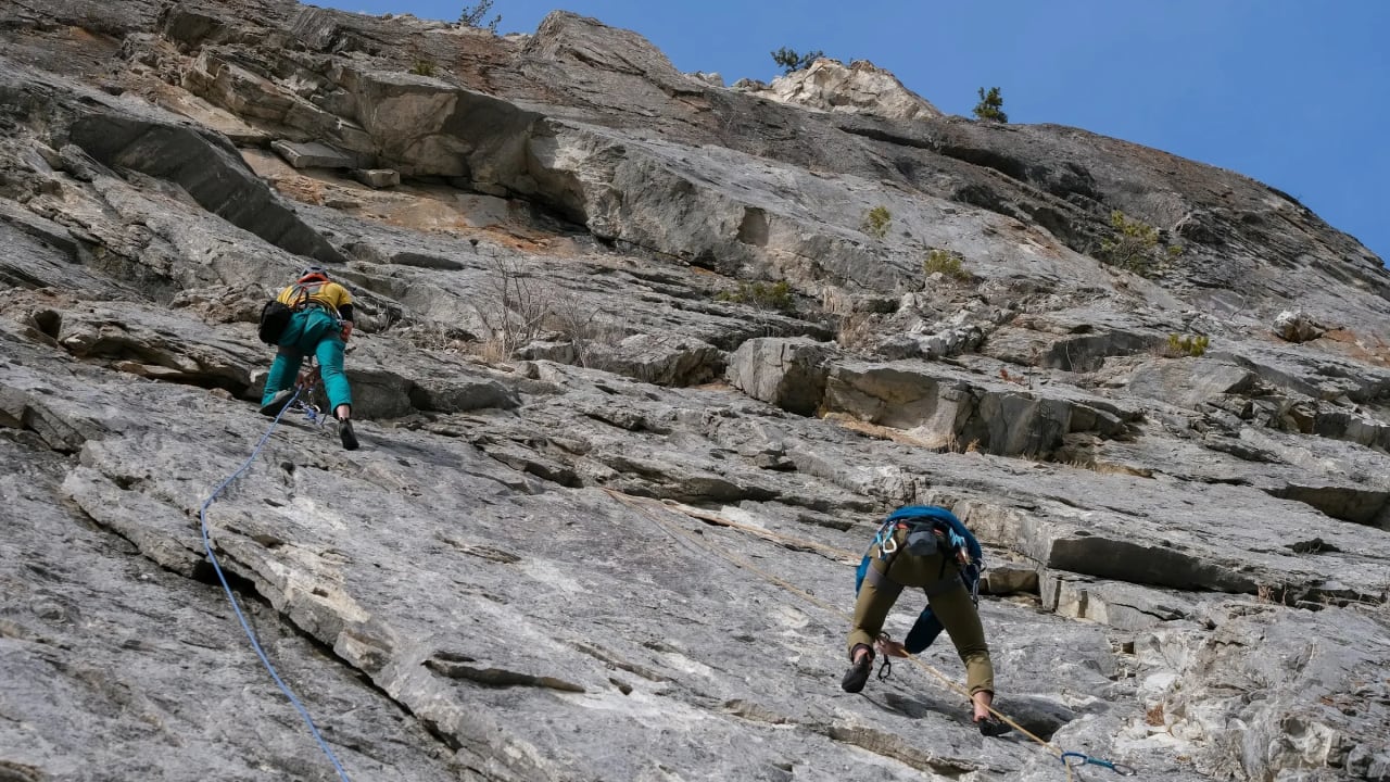 Climbers connected by rope ascending a steep rock face.