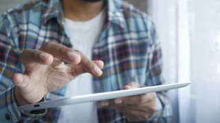 A person in a plaid shirt uses a digital tablet with a touch gesture, emphasizing the ease of technology and interactive digital communication.