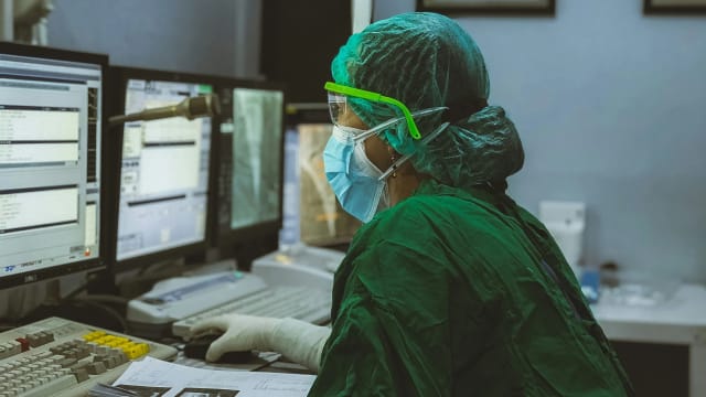 A lab technician working across a row of computer monitors in a clinical laboratory