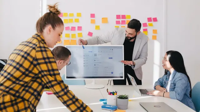 Team of professionals gathered around a computer monitor, engaged in the exploration of a new software product, with a whiteboard in the background.