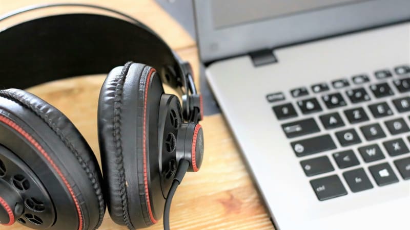 Headphones resting next to a laptop on a wooden desk symbolize the convenience of downloading music from Spotify for offline listening.