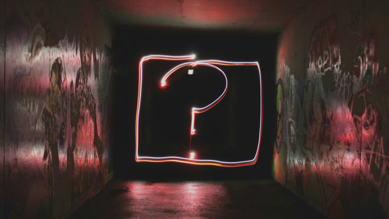 Neon question mark glowing in a dark urban tunnel with graffiti-covered walls, symbolizing the search for answers and direction in the uncertain journey of startups.