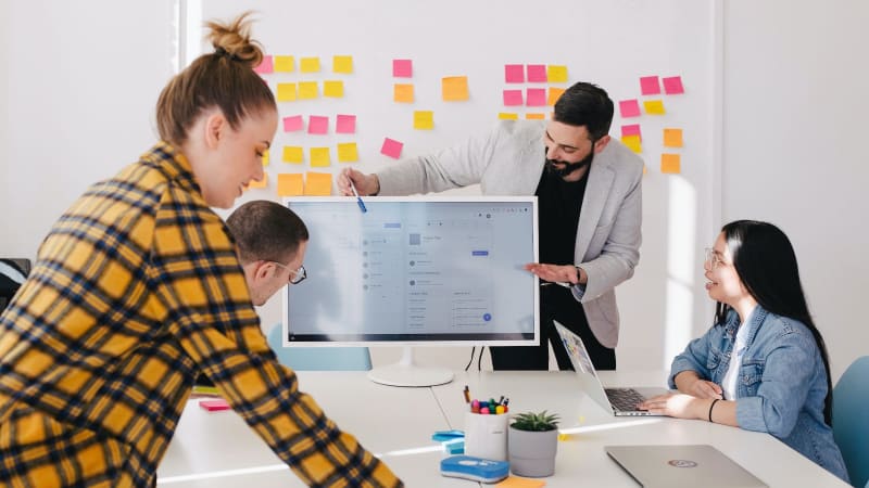 Team of professionals gathered around a computer monitor, engaged in the exploration of a new software product, with a whiteboard in the background.