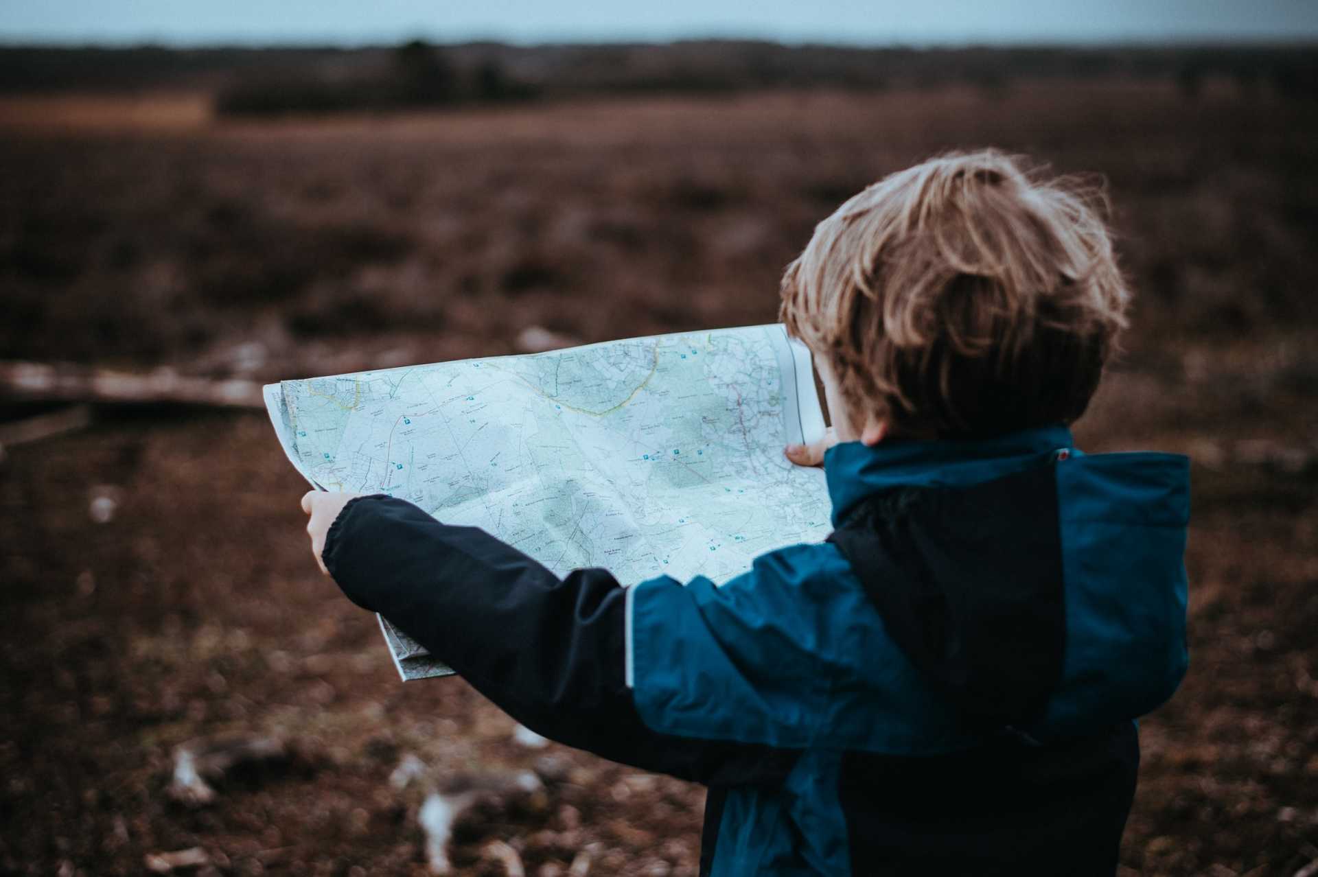 Young boy wearing a rain jacket holds up and looks at a map