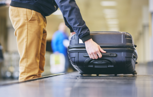 property management app image: man wearing khaki pants and long black sleeve shirt picking a black hardshell suitcase up off an airport turnstile