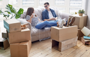 inherited tenants image: image of a young female and male sitting on a couch surrounded by moving boxes and chatting