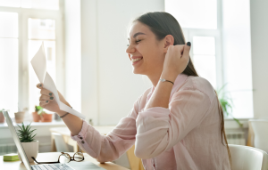 tenant screening process image: photo of woman with long brown hair holding papers in one hand and celebrating with a "Yes!" gesture