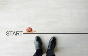 rental business snail image: picture of a man's feet in black dress shoes standing at a "start" line with a snail crawling across it
