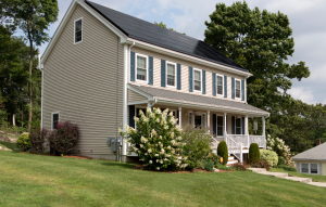 long-term rental property image of yellow house with front porch and green grass with a lilac bush