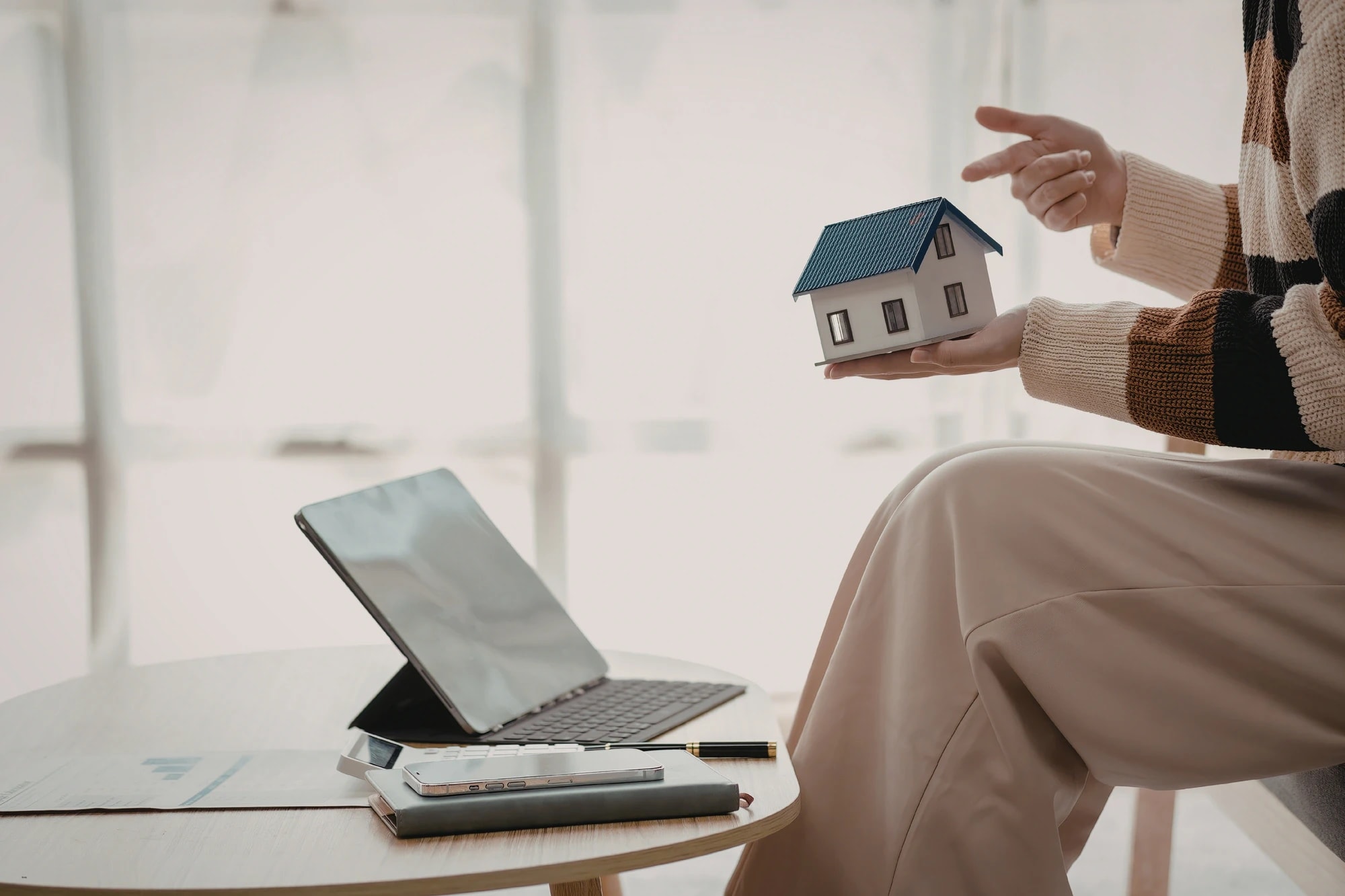 Online property management software displayed with a person holding a house model beside a laptop and smartphone.