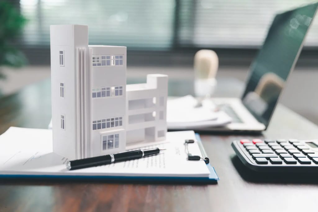 rental management architectural building model on documents beside laptop and calculator in office setting