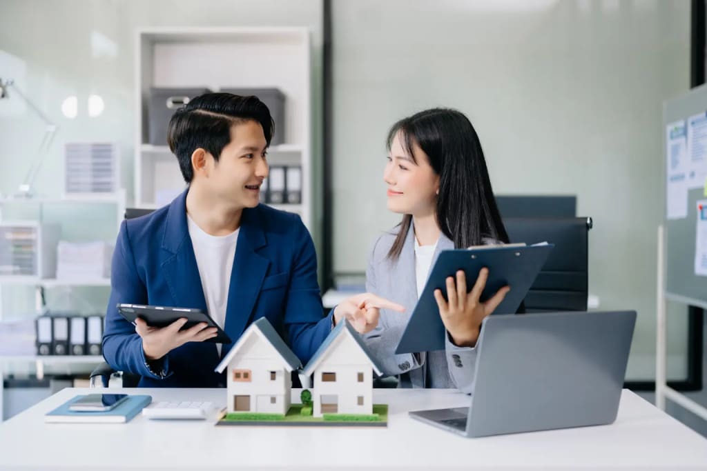 Rental property management software illustrated by a couple discussing real estate with house models and laptops.