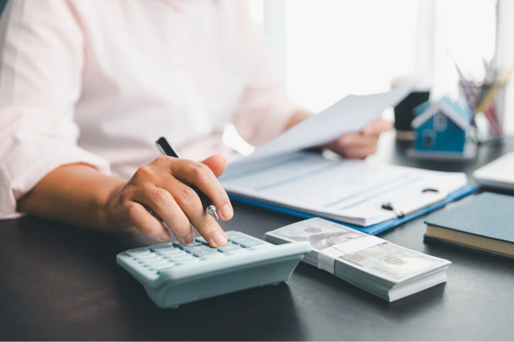 Residential property management software shown with someone calculating finances beside money and property documents.