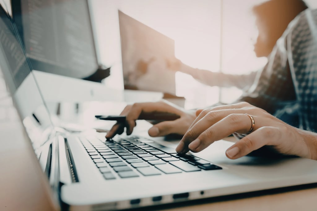 Rent tracking software: Close-up of hands typing on a laptop in a modern office, with another workstation blurred in the background.