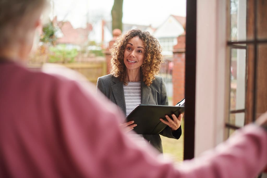 Bookkeeping for landlords illustrated by a real estate agent reviewing documents with homeowners at the front door.