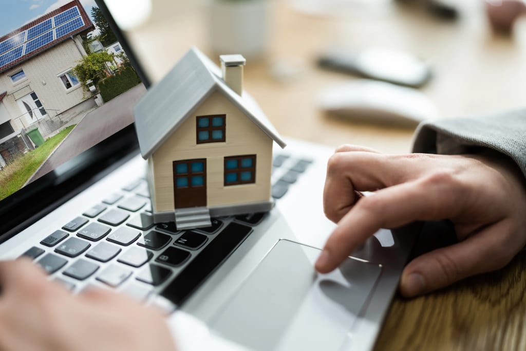 miniature house sits on a laptop keyboard as a user navigates listings, tracking rental finances digitally.