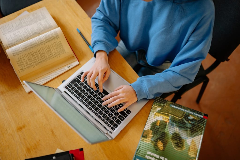 person typing on laptop using property management software with reference books on desk