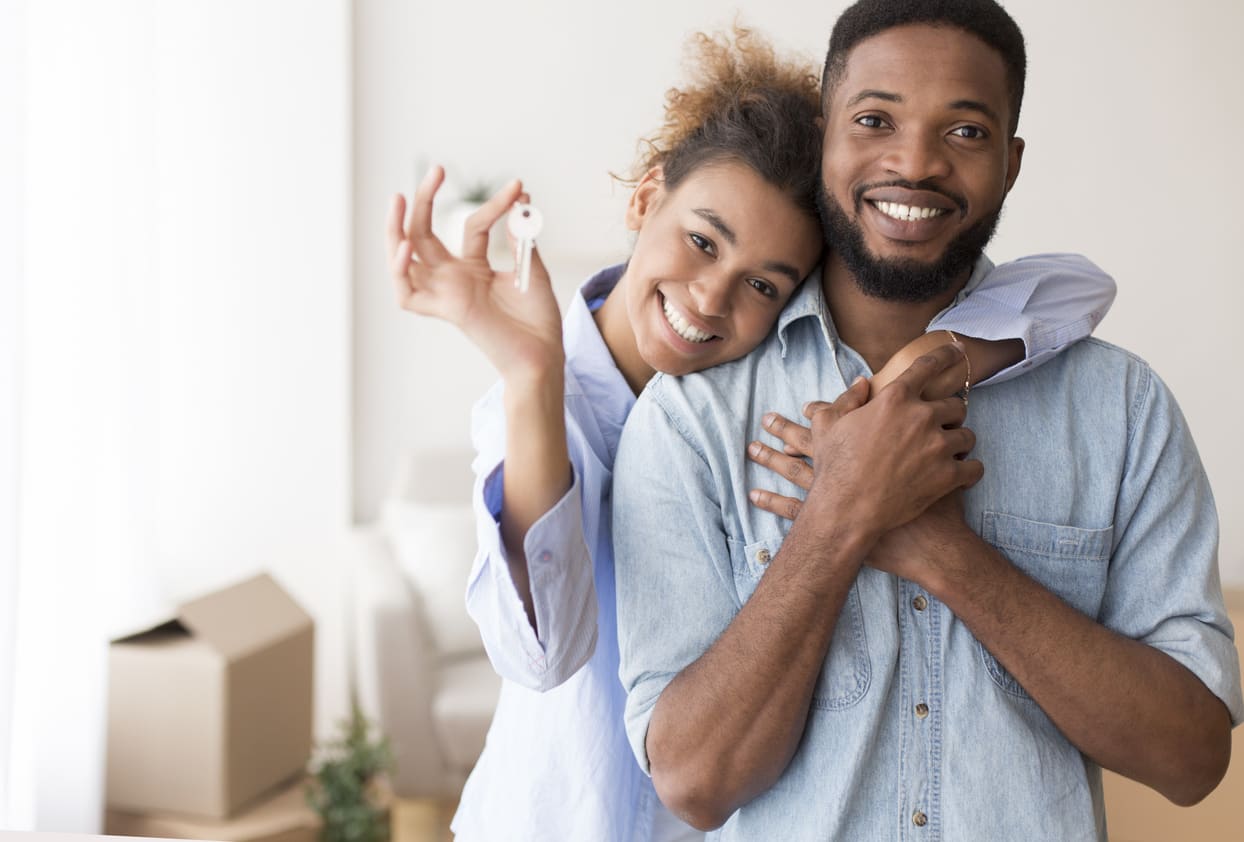 month-to-month rentals blog post hero image: young couple hugging & holding out rental property house keys