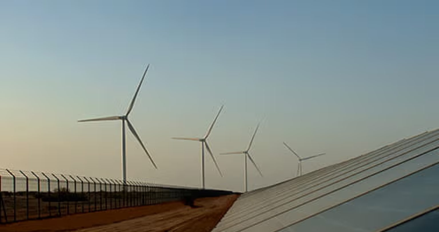 Wind turbines standing beside a row of solar panels at dusk
