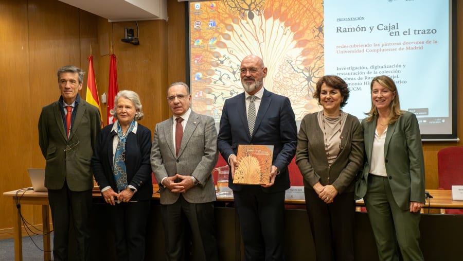 Group of five individuals standing in front of a presentation screen, holding a book titled 