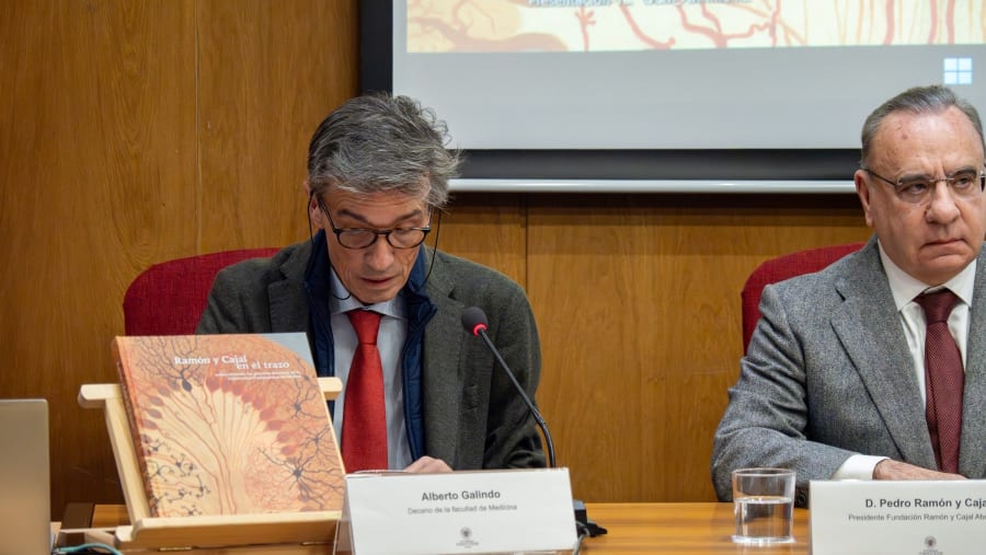 A man reading from a document at a conference table, with a book titled 