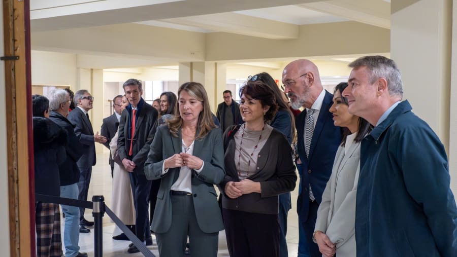 A group of people engaged in conversation in a well-lit indoor space, with a few individuals in suits and others in casual outfits, appearing to discuss an exhibit or presentation.