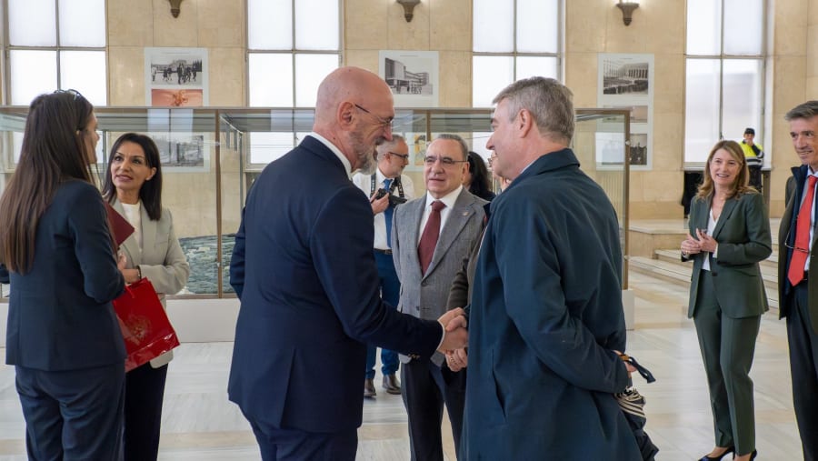 Group of professionals engaged in conversation at a formal event in a spacious hall, with historical photographs displayed on the walls.