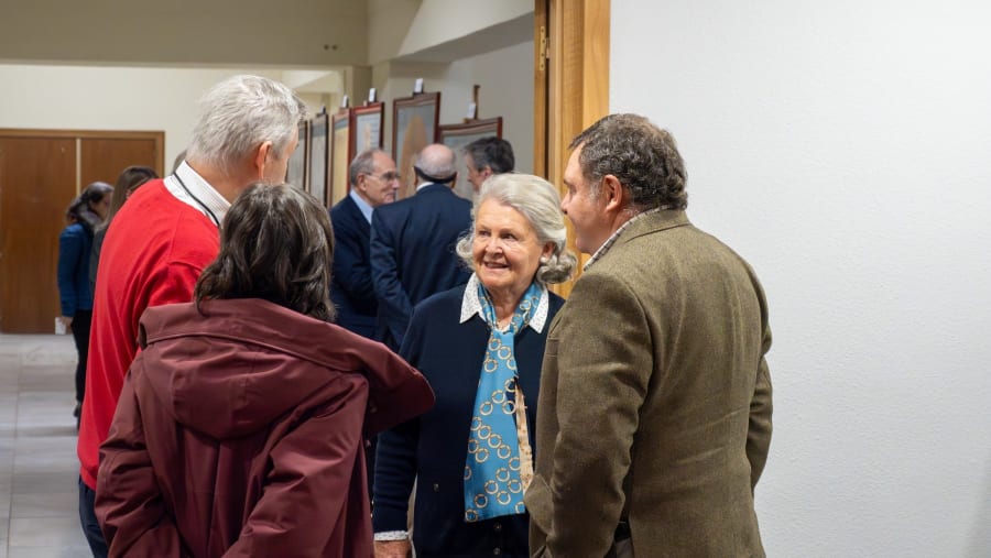 A group of people engaging in conversation in a gallery setting, with art pieces displayed in the background.