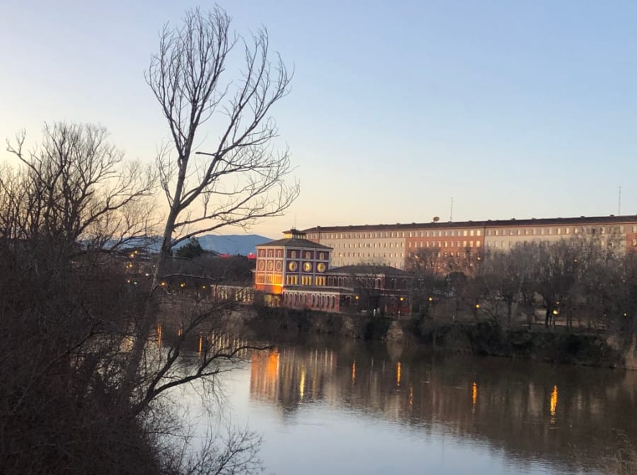 Una imagen del río con un edificio de colores al atardecer, rodeado de árboles y montañas al fondo.