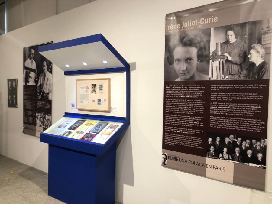 Exhibición de la biografía de Irène Joliot-Curie, con paneles informativos y objetos de archivo sobre su vida y logros, en una exposición dedicada a María Sklodowska-Curie.
