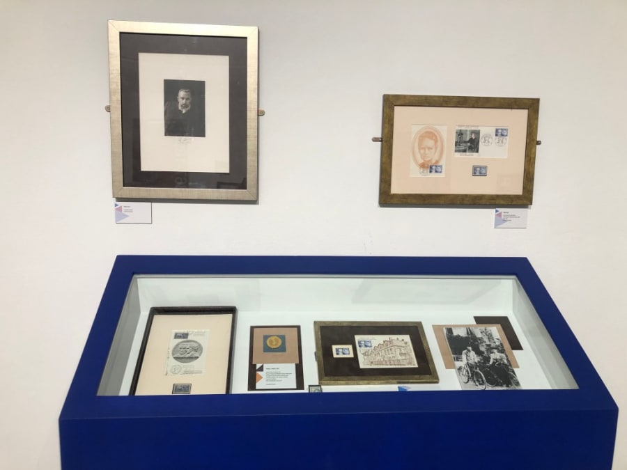 Exhibición de documentos y piezas relacionadas con María Sklodowska-Curie, incluyendo retratos enmarcados y objetos en una vitrina de exhibición azul.