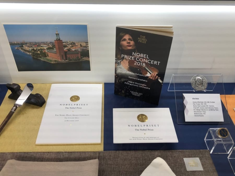 Exhibición de objetos relacionados con el Premio Nobel, incluyendo folletos, una medalla y un programa del concierto de premiación de 2018, con un fondo de la ciudad de Estocolmo.