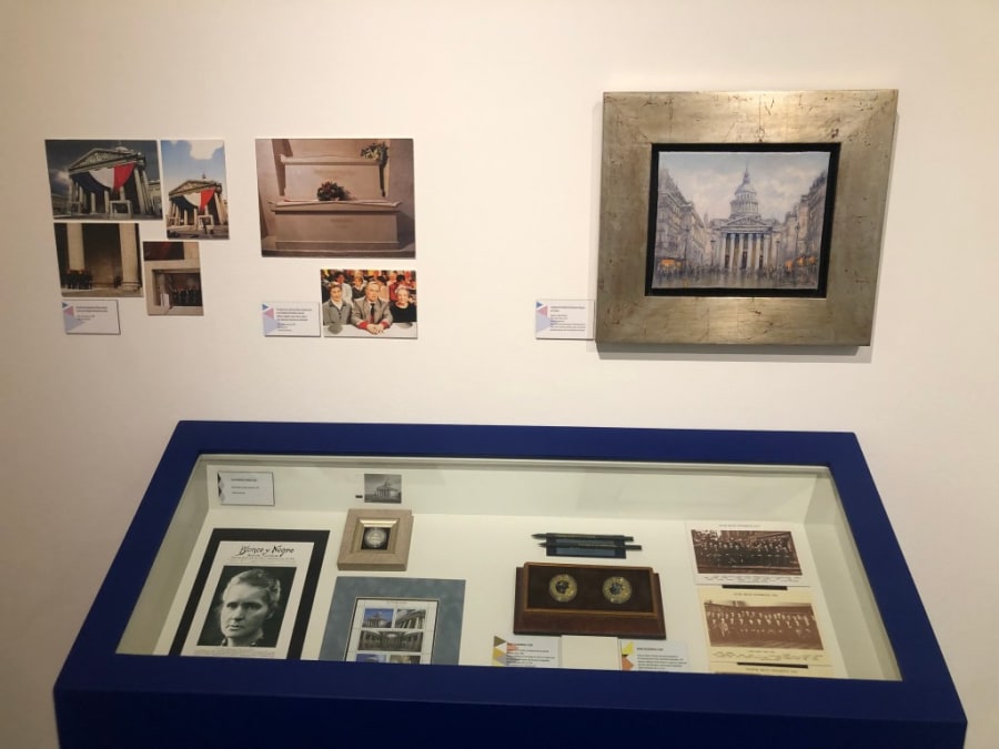 Exposición sobre María Sklodowska-Curie, con fotografías y documentos enmarcados, junto a una vitrina que exhibe objetos relacionados con su vida y logros.