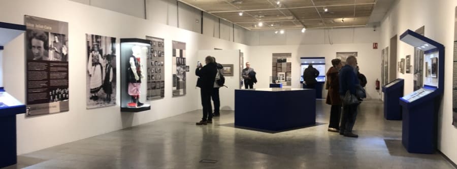 Exposición sobre María Sklodowska-Curie, mostrando paneles informativos y vitrinas con objetos relacionados. Visitantes observan la muestra en un ambiente cultural.